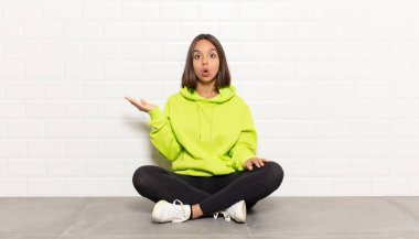 İspanyol kadın şaşırmış ve şoka uğramış görünüyor, çenesi düşmüş, eli açık bir objeyi tutuyor.