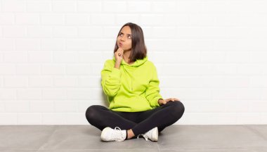 Hispanik kadın düşünceli, meraklı ya da hayal kuruyor, hayal kuruyor ve mekanı kopyalamak için yukarı bakıyor.