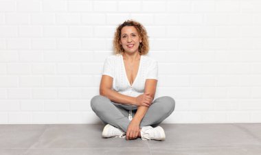 Orta yaşlı bir kadın utangaç ve neşeli bir şekilde gülüyor, arkadaş canlısı ve olumlu ama güvensiz bir tavırla.