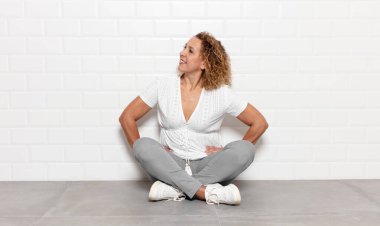 Orta yaşlı bir kadın mutlu, neşeli ve kendinden emin görünüyor. Gururla gülümsüyor ve iki elini de kalçasında istiyor.