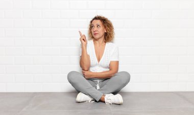 Orta yaşlı bir kadın mutlu bir şekilde gülümsüyor ve yan bakıyor, merak ediyor, düşünüyor ya da bir fikri var.