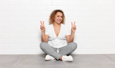 Orta yaşlı kadın gülümsüyor ve mutlu görünüyor, arkadaş canlısı ve memnun, zafer ya da barış işareti yapıyor iki eliyle