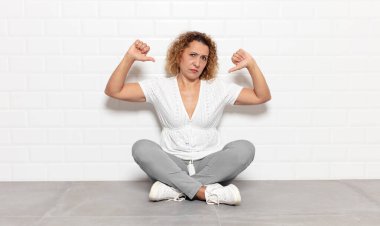 Orta yaşlı bir kadın üzgün, hayal kırıklığına uğramış ya da kızgın görünüyor. Anlaşmazlıkta baş parmağını gösteriyor. Hayal kırıklığına uğramış hissediyor.