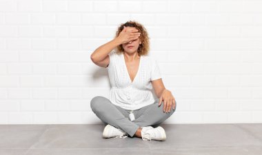 Orta yaşlı bir kadın tek eliyle gözlerini kapatıyor korkmuş ya da endişeli hissediyor, merak ediyor ya da körü körüne bir sürpriz bekliyor.