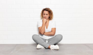 Orta yaşlı kadın ciddi, düşünceli ve endişeli, elleri çenesine bastırılmış bir şekilde yan bakıyor.