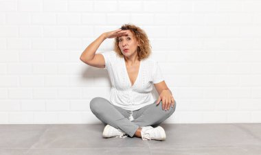 Orta yaşlı kadın şaşkınlık ve şaşkınlık içinde bakıyor. Alnı açık, uzaklara bakıyor, izliyor ya da arıyor.