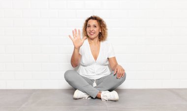 Orta yaşlı bir kadın gülümsüyor ve arkadaş canlısı görünüyor. 5 ya da 5 numarayı gösteriyor.