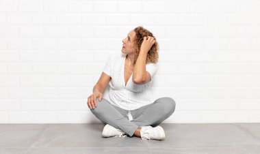 Orta yaşlı kadın düşünüyor ya da şüphe ediyor, kafasını kaşıyor, şaşkın ve kafası karışık hissediyor, geriye ya da arkaya bakıyor.