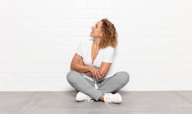 Orta yaşlı bir kadın neşeyle gülümsüyor, mutlu, tatmin olmuş ve rahatlamış hissediyor, kollarını kavuşturup yan tarafa bakıyor.