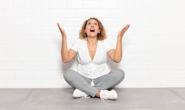 Orta yaşlı bir kadın kendini mutlu, şaşkın, şanslı ve şaşırmış hissediyor. Zaferi iki eli havada kutluyor.