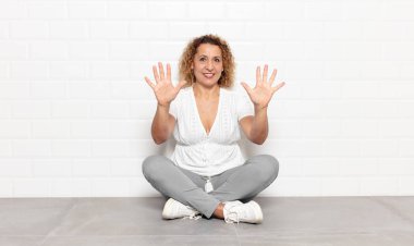 Orta yaşlı bir kadın gülümsüyor ve arkadaş canlısı görünüyor, onuncu veya onuncu numarayı gösteriyor, eli önde, geriye doğru sayıyor.