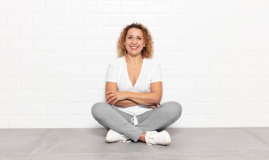 Orta yaşlı bir kadın mutlu, gururlu ve tatmin olmuş görünüyor. Kollarını kavuşturup gülümsüyor.