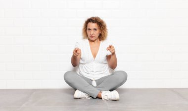 Orta yaşlı bir kadın kameraya iki parmağını ve kızgın bir ifadeyle bakarak sana görevini yapmanı söylüyor.