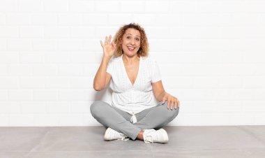 Orta yaşlı bir kadın kendini başarılı ve tatmin olmuş hissediyor ağzı açık gülümsüyor, elle işaret veriyor.