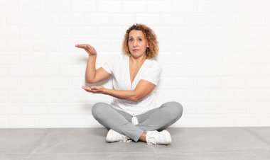 Orta yaşlı bir kadın bir objeyi iki eliyle fotokopi alanında tutuyor, bir objeyi gösteriyor, sunuyor ya da reklamını yapıyor.