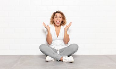 Orta yaşlı bir kadın mutlu ve heyecanlı görünüyor. Beklenmedik bir sürprizle şoke olmuş. İki eli yüzü açık.