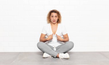 Orta yaşlı bir kadın, şaşkın ve tuhaf bakışlarıyla kendini işaret ediyor. Seçildiğine şaşırmış ve şaşırmış.