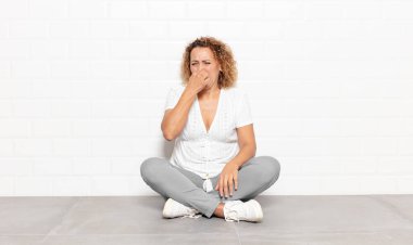 Orta yaşlı bir kadın iğrenç ve nahoş bir koku almaktan kaçınmak için burnunu tutuyor.