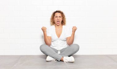 Orta yaşlı bir kadın sinirli bir ifadeyle ya da yumruklarıyla başarıyı kutlarken agresif bir şekilde bağırıyor.