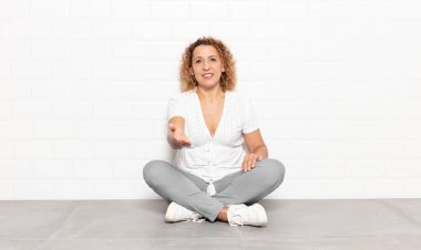 Orta yaşlı bir kadın gülümsüyor, mutlu, kendinden emin ve arkadaş canlısı görünüyor, bir anlaşmaya varmak için el sıkışmayı teklif ediyor, işbirliği yapıyor.