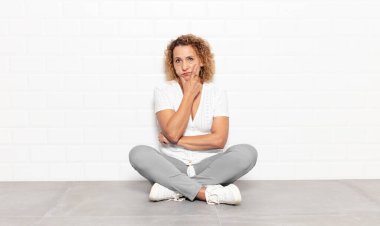 Orta yaşlı bir kadın ciddi, düşünceli ve güvensiz görünüyor, bir kolu çapraz ve çenesi üzerinde, seçenekleri tartıyor.