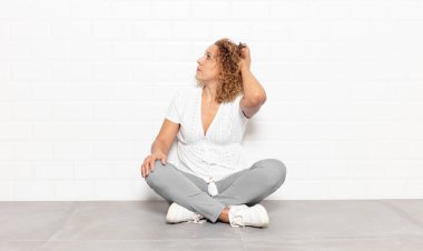 Orta yaşlı bir kadın bilgisiz ve kafası karışık, bir çözüm düşünüyor, eli kalçasında, diğeri kafasında, dikiz aynasından.