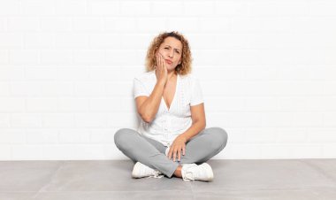 Orta yaşlı bir kadın yanağını tutuyor ve ağrılı diş ağrısı çekiyor. Hasta, sefil ve mutsuz hissediyor. Dişçi arıyor.