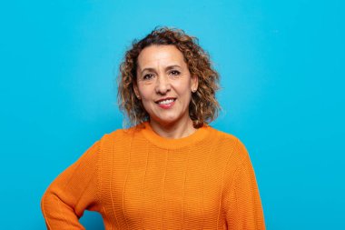 Orta yaşlı bir kadın mutlu bir şekilde gülümsüyor. Kendine güvenen, olumlu, gururlu ve arkadaş canlısı bir tavırla.