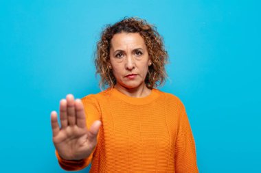 Orta yaşlı bir kadın ciddi, sert, hoşnutsuz ve kızgın görünüyor.