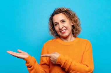 Orta yaşlı kadın gülümsüyor, mutlu, kaygısız ve tatmin olmuş hissediyor, fotokopi alanındaki konsepte veya fikre işaret ediyor.