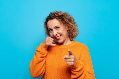 Orta yaşlı bir kadın neşeli bir şekilde gülümsüyor ve kamerayı işaret ediyor. Sonra seni arıyor, telefonla konuşuyor.