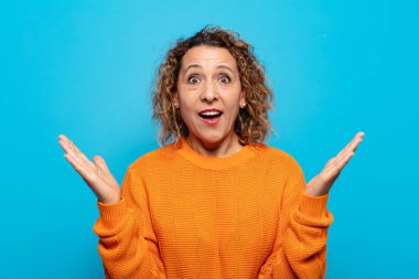 Orta yaşlı bir kadın mutlu, heyecanlı, şaşırmış ya da şaşırmış hissediyor, gülümsüyor ve hayret verici bir şeye şaşırıyor.