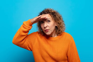 Orta yaşlı kadın şaşkınlık ve şaşkınlık içinde bakıyor. Alnı açık, uzaklara bakıyor, izliyor ya da arıyor.