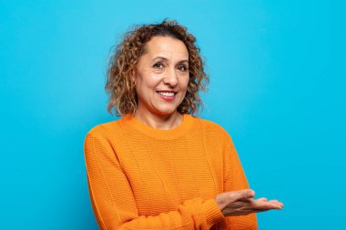 Orta yaşlı bir kadın neşeli bir şekilde gülümsüyor, mutlu hissediyor ve fotokopi alanında bir konsept gösteriyor.