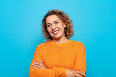 Orta yaşlı bir kadın kollarını kavuşturup mutlu bir şekilde gülüyor, rahat, pozitif ve tatmin edici bir pozla.