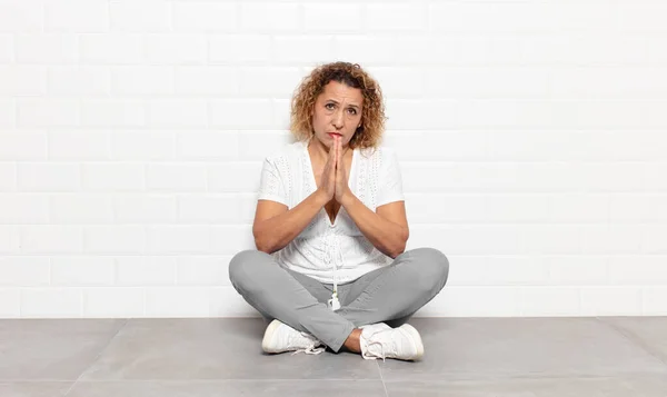 middle age woman feeling worried, hopeful and religious, praying faithfully with palms pressed, begging forgiveness