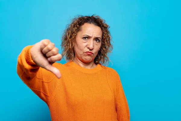 Orta yaşlı bir kadın sinirli, sinirli, hayal kırıklığına uğramış ya da canı sıkkın, ciddi bir bakışla başparmağını kaldırıyor.