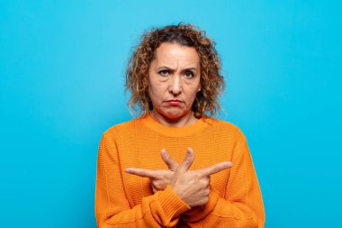 Orta yaşlı kadın şaşkın ve şaşkın görünüyor, güvensiz ve şüpheyle zıt yönleri işaret ediyor.