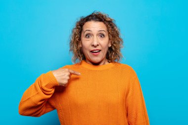 Orta yaşlı kadın mutlu, gururlu ve şaşırmış görünüyor, neşeli bir şekilde kendini gösteriyor, kendinden emin ve kibirli hissediyor.