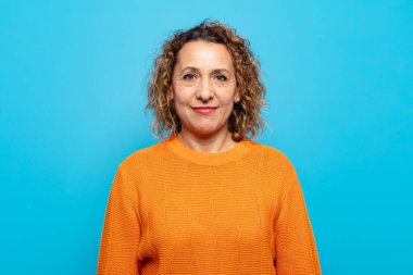 Orta yaşlı kadın pozitif ve kendinden emin gülümsüyor. Tatmin olmuş, arkadaş canlısı ve mutlu görünüyor.