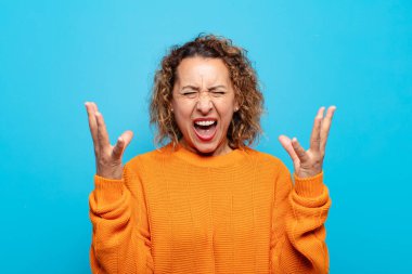 Orta yaşlı bir kadın öfkeyle bağırıyor, stresli hissediyor ve ellerini havaya kaldırıp neden ben diye bağırıyor.