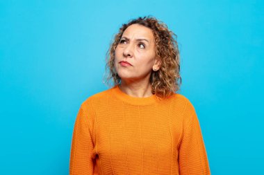 Orta yaşlı kadın şaşkın ve şaşkın görünüyor, merak ediyor veya bir sorunu çözmeye çalışıyor veya düşünüyor.