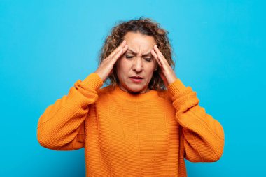 Stresli ve hayal kırıklığına uğramış görünen orta yaşlı bir kadın, baskı altında çalışıyor, başı ağrıyor ve sorunları var.