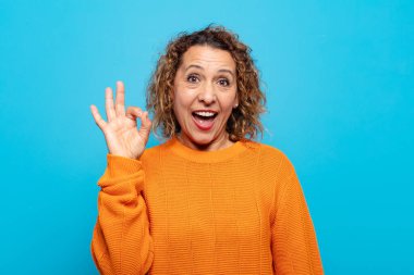 Orta yaşlı bir kadın kendini başarılı ve tatmin olmuş hissediyor ağzı açık gülümsüyor, elle işaret veriyor.