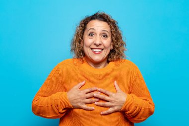 Orta yaşlı kadın mutlu, şaşırmış, gururlu ve heyecanlı görünüyor.