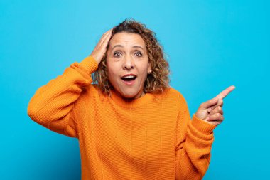 Orta yaşlı bir kadın gülüyor, mutlu, pozitif ve şaşırmış görünüyor, yanal fotokopi alanını işaret eden harika bir fikrin farkına varıyor.