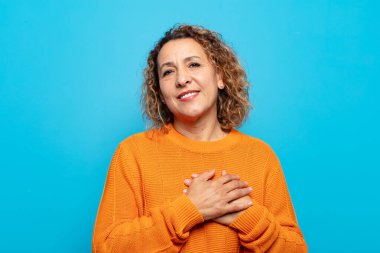 Orta yaşlı bir kadın romantik, mutlu ve aşık, neşeli bir şekilde gülümseyen ve kalbe yakın el ele tutuşan