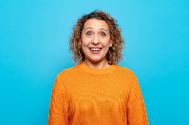 Orta yaşlı bir kadın mutlu ve hoş bir şekilde şaşırmış görünüyor. Büyülenmiş ve şok olmuş bir ifadeyle heyecanlanıyor.