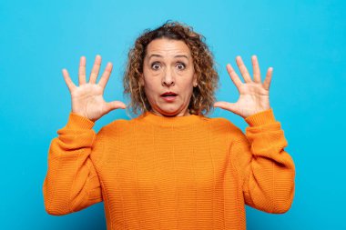 Orta yaşlı bir kadın elleri havada bağırıyor. Öfkeli, sinirli, stresli ve üzgün.