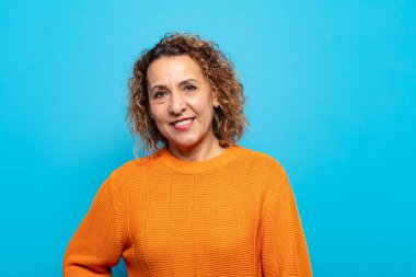 Orta yaşlı bir kadın mutlu, mutlu, kendinden emin ve rahat bir ifadeyle neşeli bir şekilde gülümsüyor.